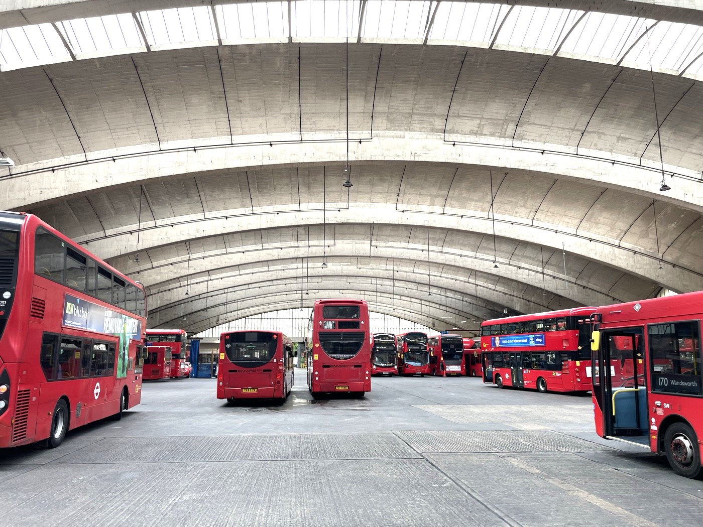 London bus depot with fleet of red double-decker electric buses under arched canopy