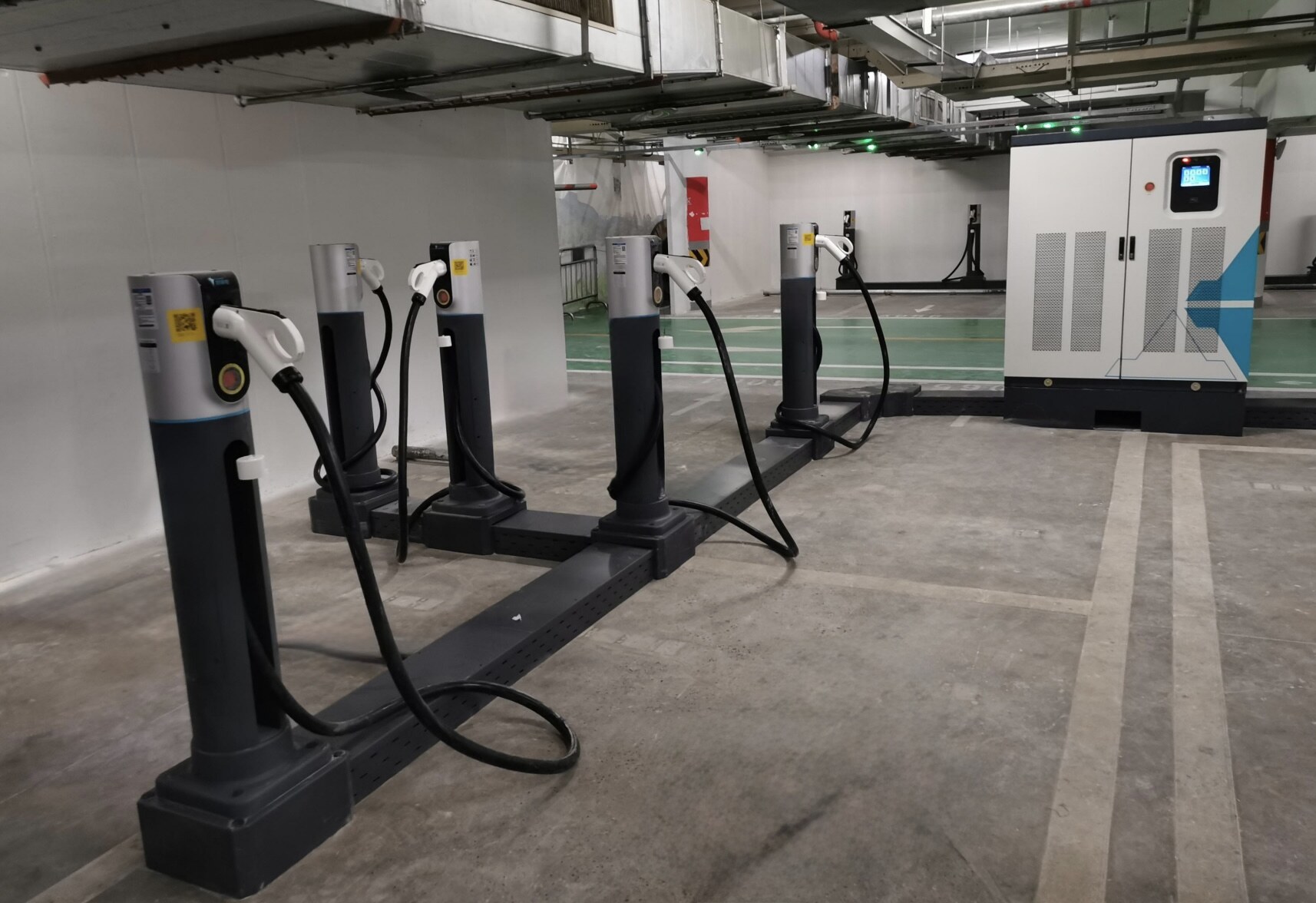 Row of rapid deployment EV charger dispensers on surface-mounted bases connected to a freestanding power cabinet inside an indoor car park, installed without excavation
