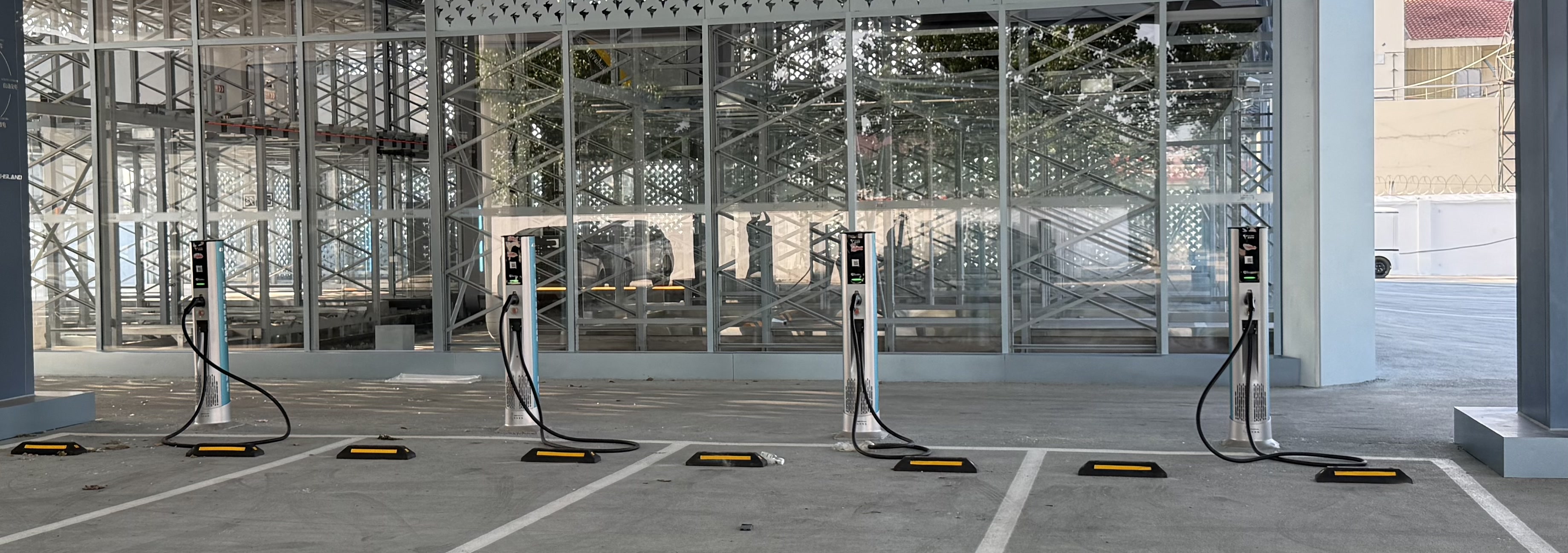 Row of Neutron DC Satellite Terminal chargers on yellow parking stops in front of a glass-facade commercial building